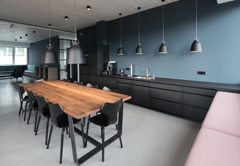 Modern kitchen with a matte blue painted wall, sleek black painted cabinetry, 10 seat dining table with a fine wood top