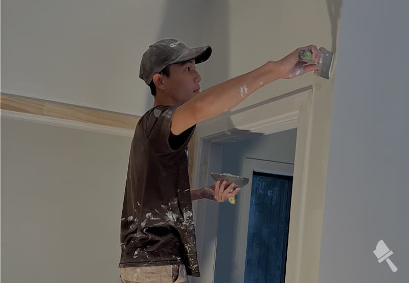 Professional painter on top of a step ladder, plastering an interior wall corner to prepare it for painting