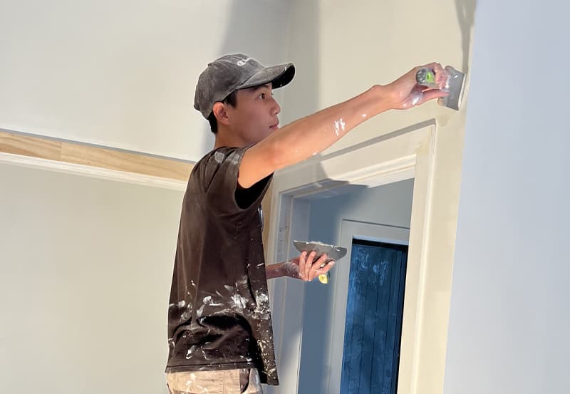 Professional painter on top of a step ladder, plastering an interior wall corner to prepare it for painting
