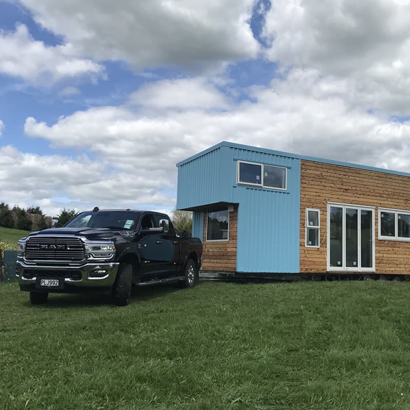 Black Ram truck towing a larger tiny home in a rural area, ready to take it to it's next location