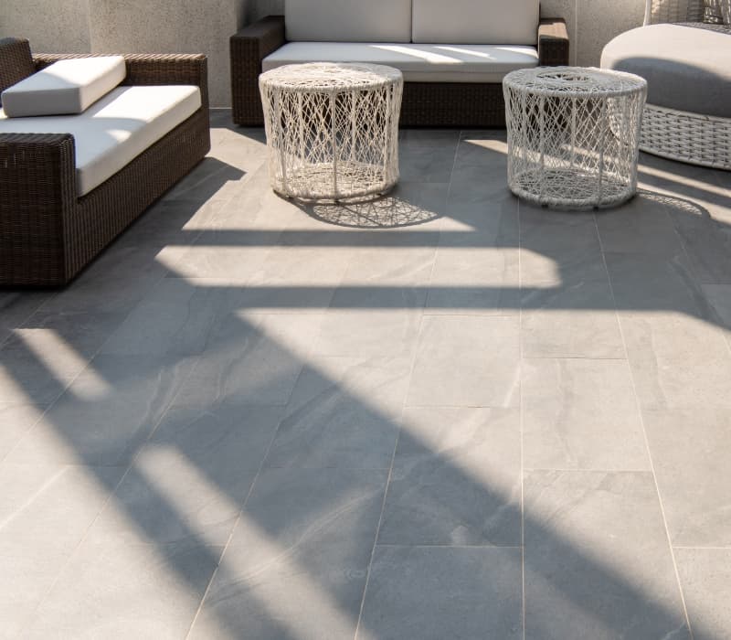 Outdoor seating area with a grey porcelain tile floor and white and dark grey outdoor furniture