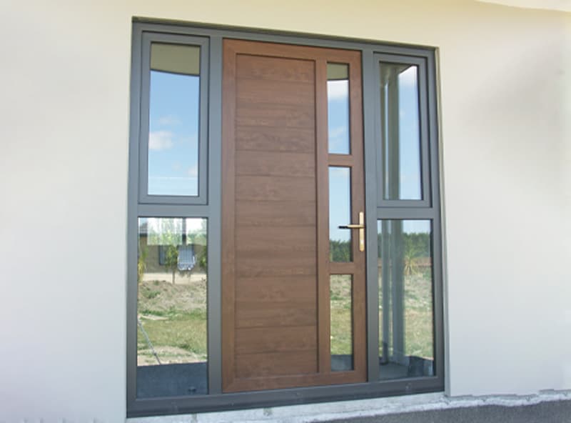 Brown front door with little vertical windows on either side, all with black uPVC framing