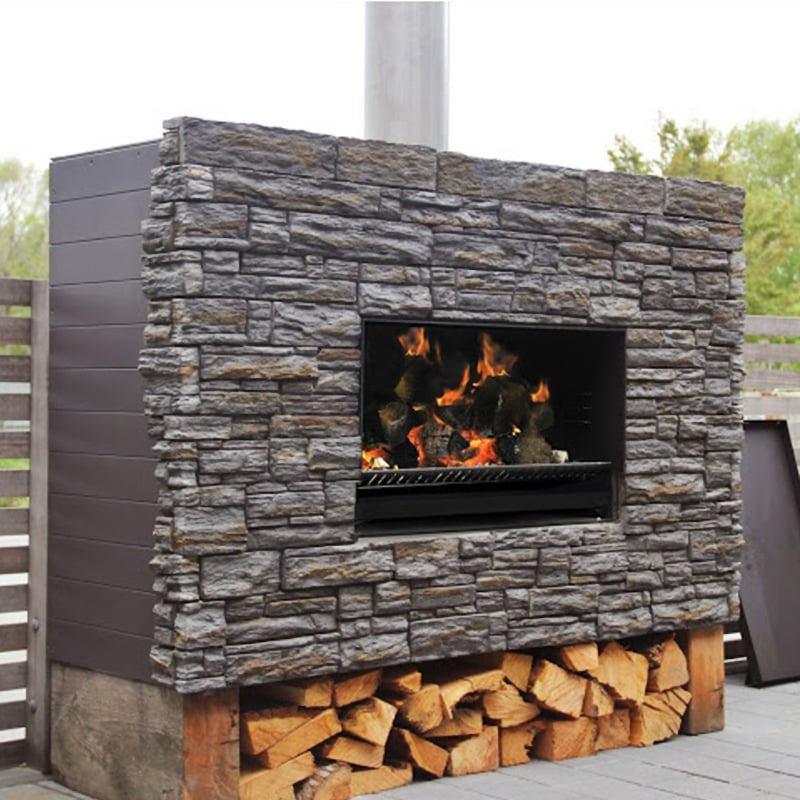 Outdoor fireplace that sits in rectangular weatherboard housing with a stone front and firewood stored below