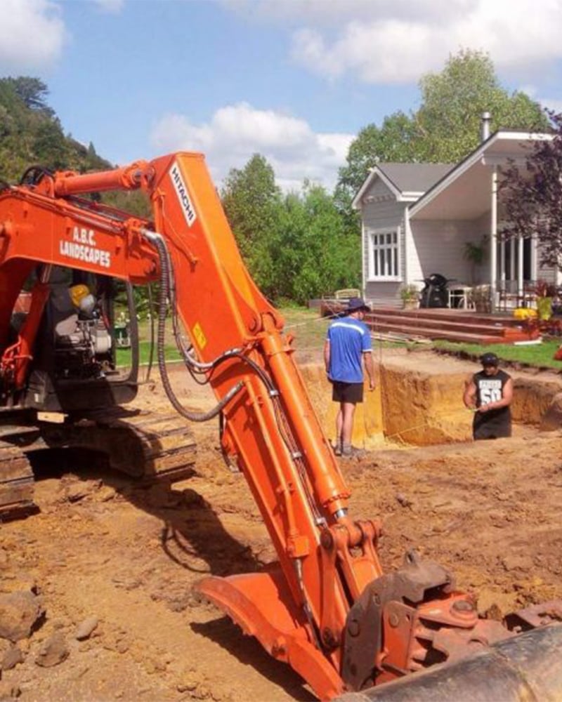 The ABC Excavation and landscaping team with a Vibrant orange digger excavating earth in a residential property's backyard