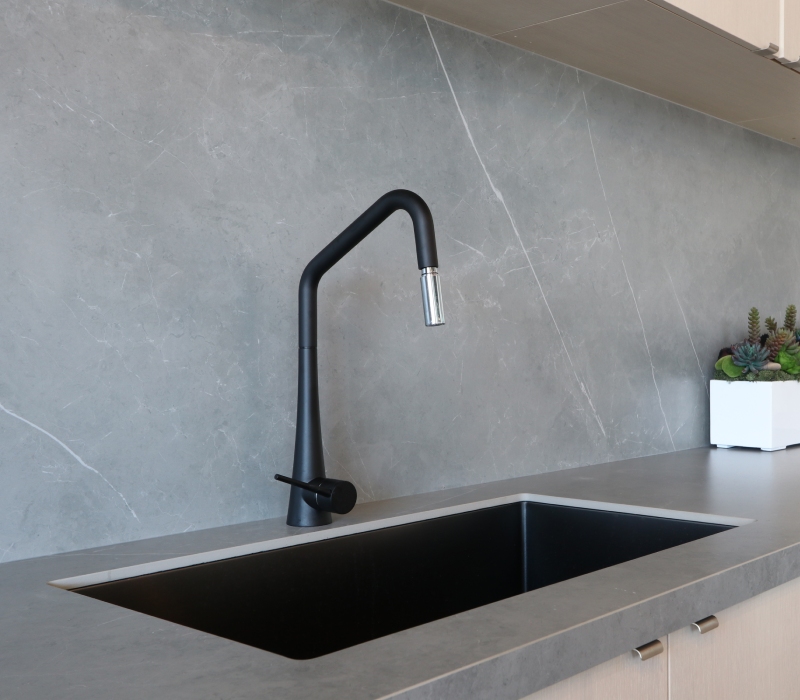 Grey porcelain kitchen benchtop with a sleek black sink and tap and a white container with heaps of succulents