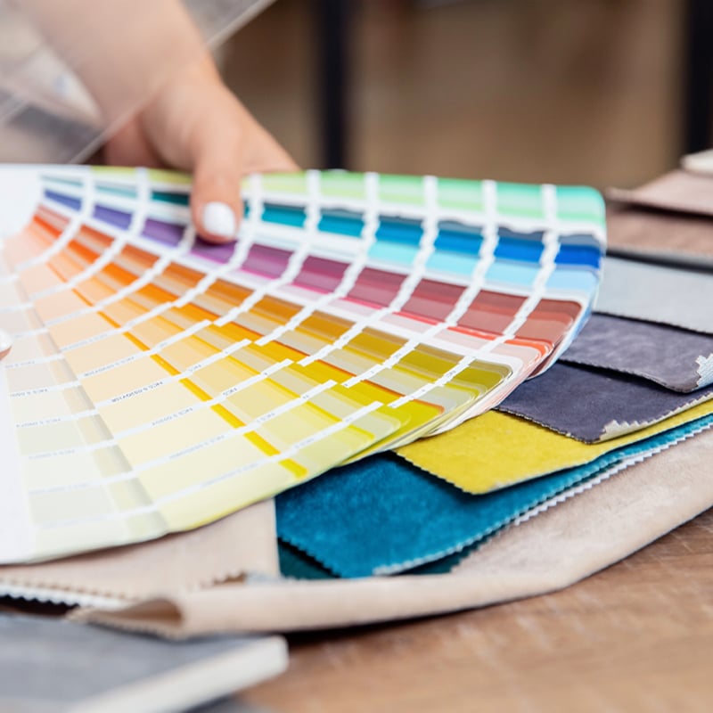 Woman with nicely painted white nails holding an array of colour sheets for matching and contrasting colours to fabric for their home