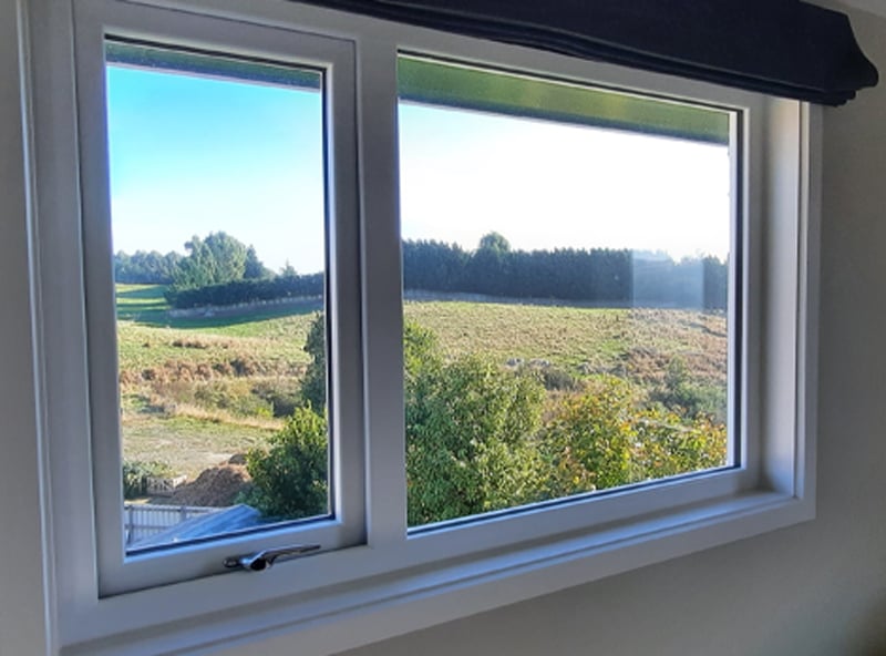 White uPVC window frame from the inside of a rural house that shows the outside view with lines of trees and large fields
