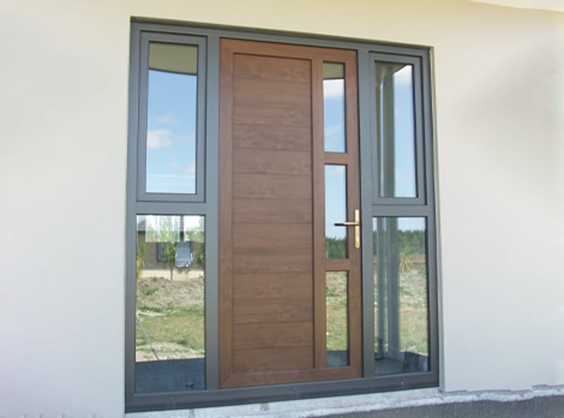 Brown front door with little vertical windows on either side, all with black uPVC framing