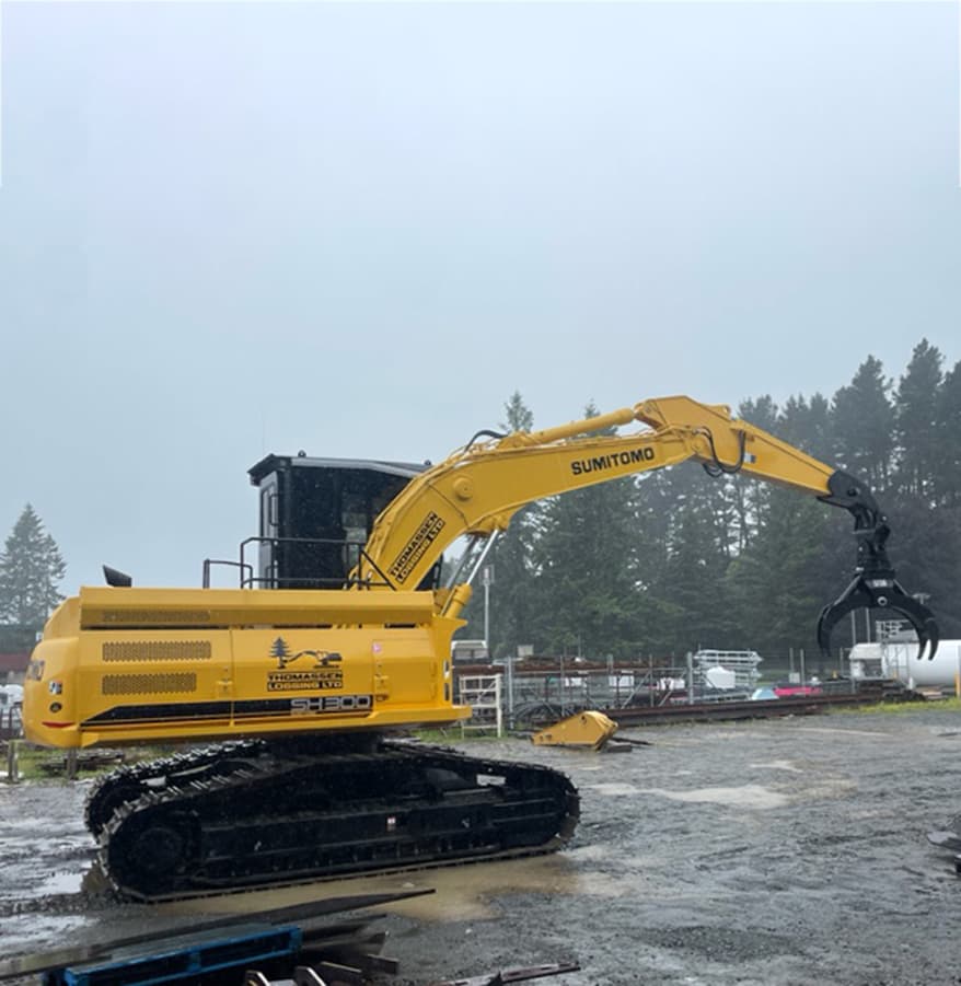 Medium sized yellow digger with a claw bucket attachment parked on wet gravel with surrounding grey mist