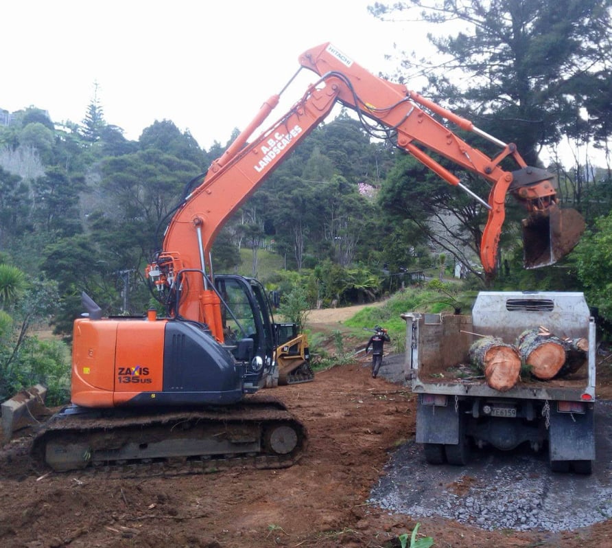 Medium-sized orange digger lifting large pieces of timber onto a truck to remove them from the site