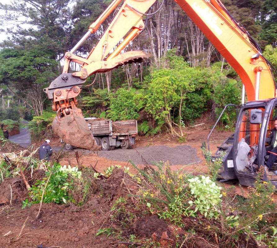 Large orange digger excavating and moving dirt and plant debris into a ABC excavating and landscaping truck