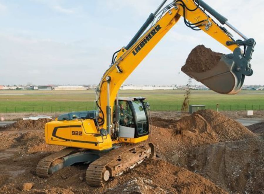 Large yellow digger excavating trenches for drainage in a field with a bucket lifted up full of dirt