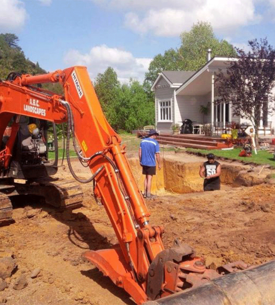 The ABC Excavation and landscaping team with a Vibrant orange digger excavating earth in a residential property's backyard