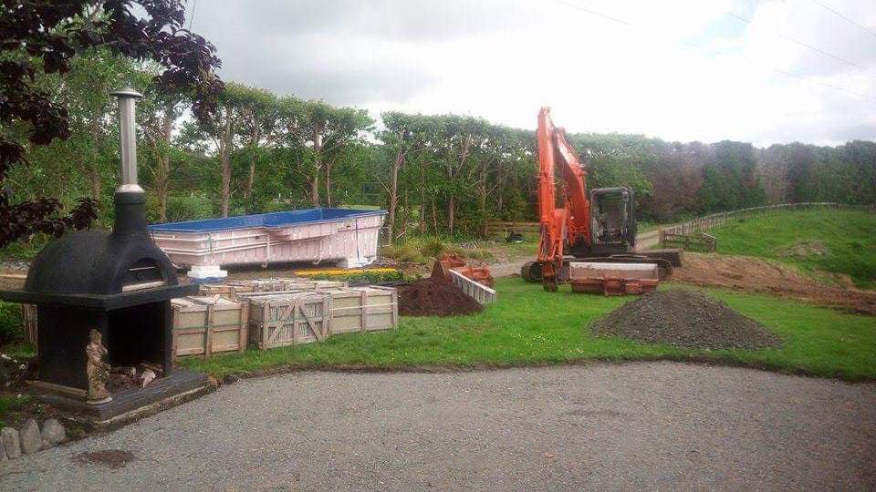 Large orange digger in a houses backyard preparing the site to lift an in-ground pool into its hole