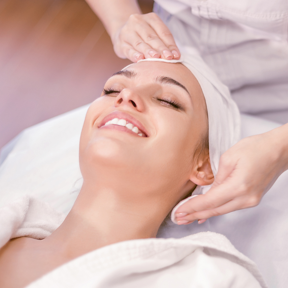 Woman laying back looking blissful and happy as she gets her forehead and side of her face rubbed with cotton pads